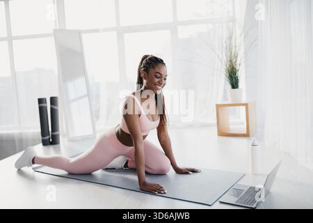 Young Woman Doing Stretches at Home While Following a Video Tutorial on Her Laptop Stock Photo