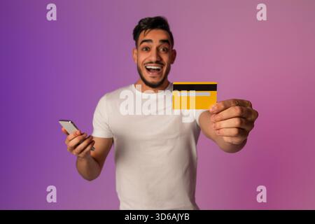Joyful Millennial Arab Man Enjoys Online Shopping Experience With Credit Card and Phone Stock Photo
