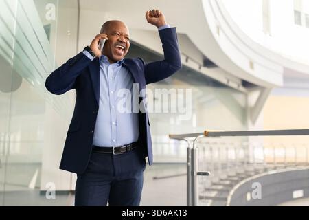 Excited mature African American businessman celebrating success while talking on cellphone Stock Photo