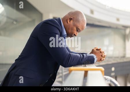 Stressed mature African American businessman leaning forward with hands clasped Stock Photo