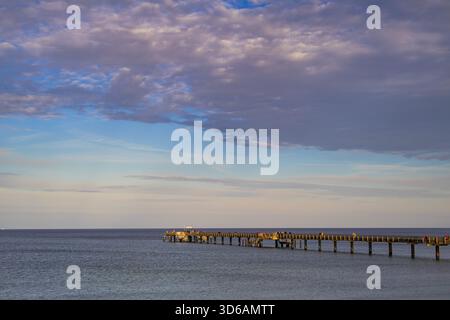 Baltic Sea pier at Binz, Rügen Island, Germany: long wooden jetty extending into calm autumn waters under a dramatic pastel-colored evening sky. Stock Photo