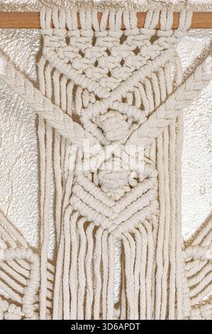 Handmade macrame wall hanging crafted with natural cotton cord, ideal for hobbyists and boho home decor. The detailed knots create a cozy and stylish Stock Photo