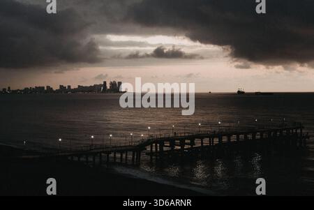 Moody, dark coastal scene featuring an illuminated pier extending into the Black Sea, with the distant modern Batumi city skyline Stock Photo