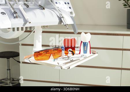 On the tray are various dental instruments, a model dental implant and bright orange safety glasses, ready for use in clinical dental settings Stock Photo