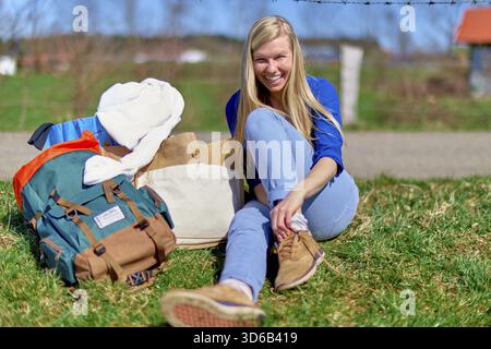 Jaunty woman with backpack taking a break during hiking trip on countryside in Bavaria, Germany, smile, happy, rural, rest, weekend, leisure activity Stock Photo
