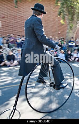 Rider in dress style of the late 1800's riding high atop a penny-farthing or high-wheel bicycle. Stock Photo