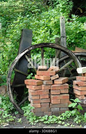 Old Wooden Wagon Wheel with Stacked Bricks in Greenery Stock Photo
