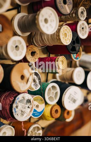 Colorful thread spools arranged on a wooden wall in a sewing studio during daylight Stock Photo