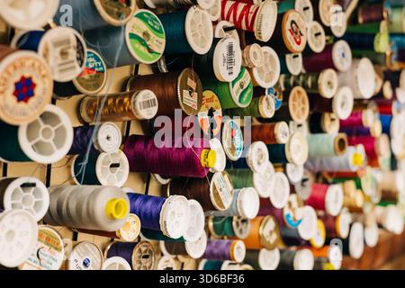Colorful thread spools neatly arranged on a wall in a sewing studio during daytime Stock Photo