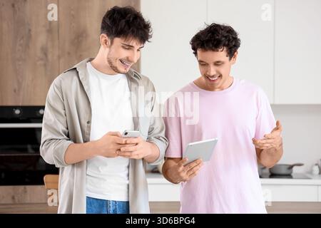Young brothers using tablet computer and mobile phone in kitchen Stock Photo