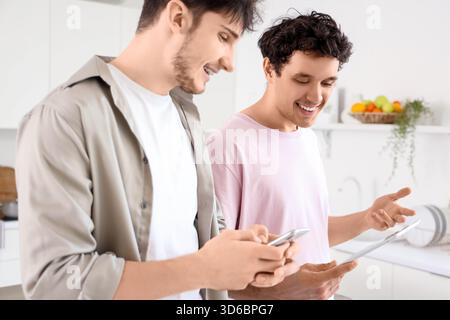 Young brothers using tablet computer and mobile phone in kitchen Stock Photo
