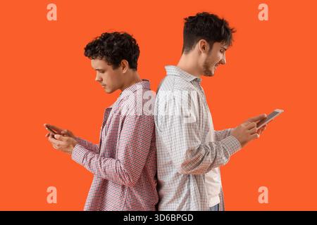 Young brothers using tablet computer and mobile phone on orange background Stock Photo