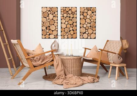 Interior of living room with armchairs, ladder and candle holders on wicker coffee table near white wall Stock Photo