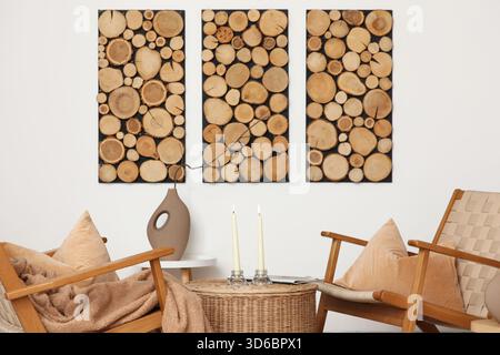 Interior of living room with armchairs and candle holders on wicker coffee table near white wall Stock Photo