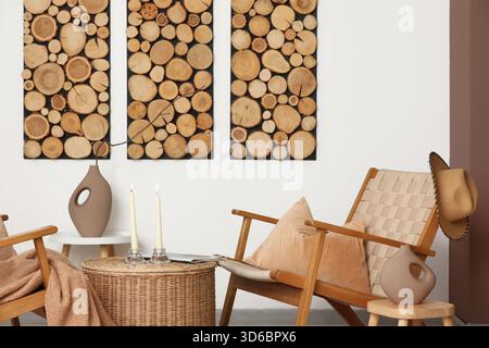 Interior of living room with armchairs and candle holders on wicker coffee table near white wall Stock Photo