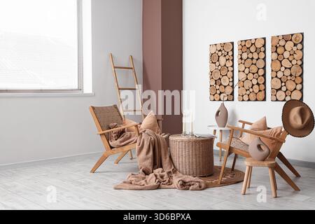 Interior of living room with armchairs, ladder and candle holders on wicker coffee table near white wall Stock Photo