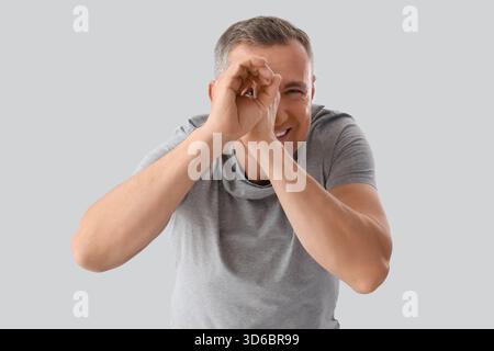 Mature man looking through imaginary telescope on light background Stock Photo