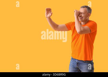 Mature man looking through imaginary spyglass on yellow background Stock Photo