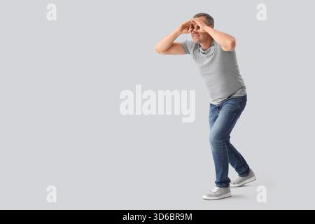 Mature man looking through imaginary binoculars on light background Stock Photo