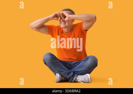 Mature man looking through imaginary binoculars on yellow background Stock Photo
