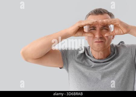 Mature man looking through imaginary binoculars on light background Stock Photo