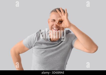 Mature man looking through imaginary telescope on light background Stock Photo