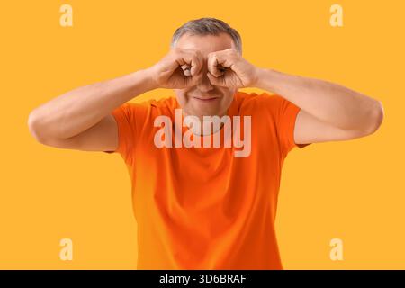 Mature man looking through imaginary binoculars on yellow background Stock Photo
