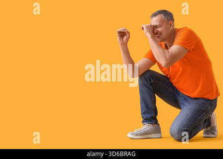 Mature man looking through imaginary telescope on yellow background Stock Photo