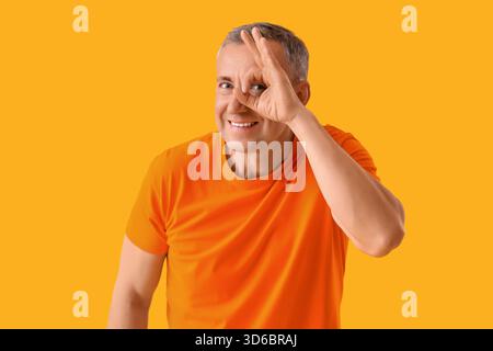 Mature man looking through imaginary telescope on yellow background Stock Photo