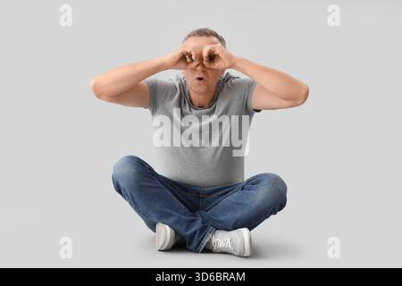 Mature man looking through imaginary binoculars on light background Stock Photo