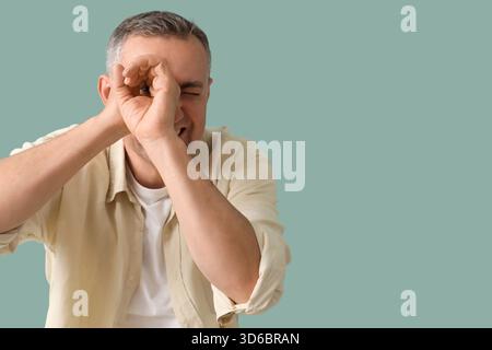 Mature man looking through imaginary telescope on green background Stock Photo