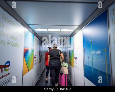 PARIS, FRANCE - JUNE 29, 2025: Passengers walk through a jet bridge lined with TotalEnergies posters showing solar panels and wind turbines while boar Stock Photo