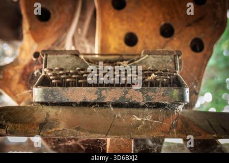 Close up of a rusty old typewriter covered in cobwebs and dust, sitting on a wooden surface, illustrating technological obsolescence and the passage o Stock Photo