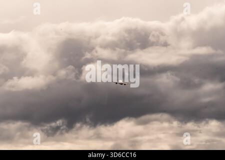 Commercial airplane climbing into dense, overcast clouds The sky is filled with dramatic, dark gray clouds, creating a moody atmosphere Stock Photo