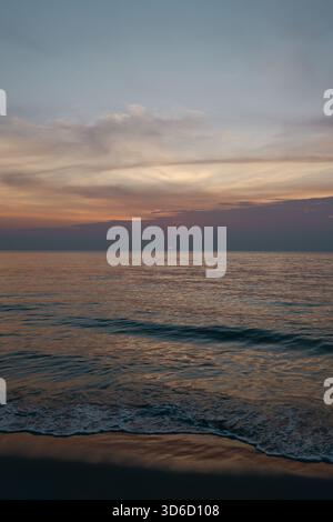 A vertically framed view of a tranquil beach with gentle waves and soft evening light, ideal for themes of relaxing coastal moments. Stock Photo