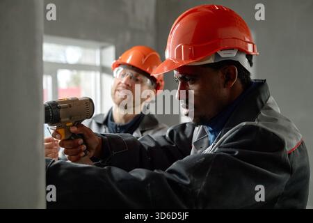 Young Adult Black Man Using Power Drill While Caucasian Man Supervising Stock Photo