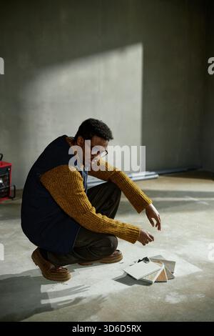 Young Adult Black Man Squatting on Floor Examining Color Swatches Stock Photo