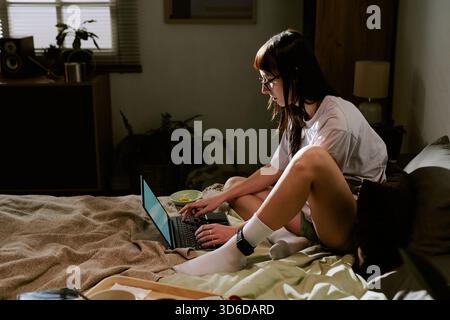 Biracial Young Adult Woman Working Remotely on Laptop Wearing Ankle Monitor Stock Photo