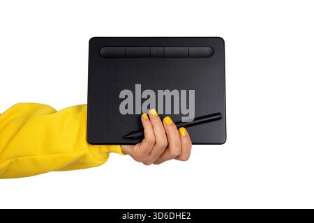 Female hand in yellow sleeve holding a black digital drawing tablet and stylus on white background. Modern creative technology concept. Stock Photo