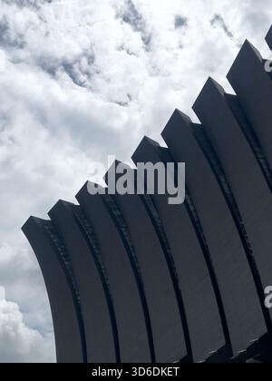 A large, contemporary building facade with a wave-like or ribbed design, viewed dramatically against an overcast sky. Stock Photo
