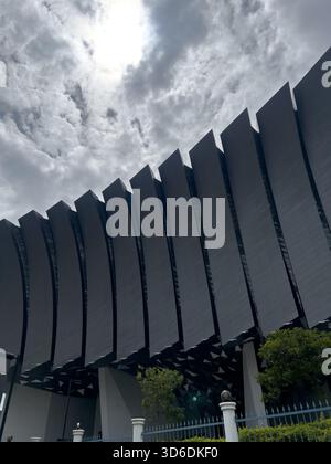 A large, contemporary building facade with a wave-like or ribbed design, viewed dramatically against an overcast sky. Stock Photo