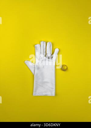 A single white dress glove, arranged flat, with a diamond crystal band ring on the middle finger, and a separate ornate gold ring placed next to it. Stock Photo