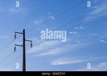 A single, simple utility pole with three power lines and insulators, set against a vast blue sky with light, wispy cirrus clouds. Minimalist look. Stock Photo