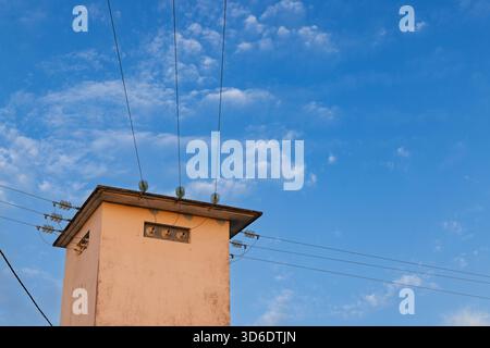 A concrete electrical transformer building, or distribution substation, with power lines and glass insulators against a soft, cloudy blue sky at dusk. Stock Photo