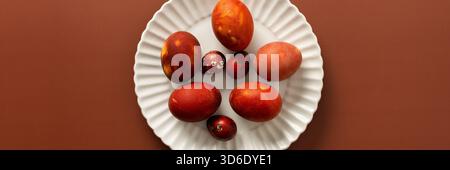 Vibrant Easter eggs in various shades of red and orange are beautifully arranged on a white plate, adding charm to the festive atmosphere of the seaso Stock Photo