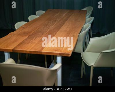 long dining or office table with wooden tabletop and a bunch of chairs in a dark room Stock Photo