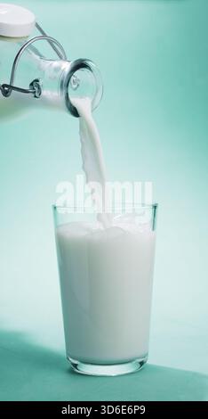 Pouring milk from a bottle of milk into the glass on light blue background.  Vertical image. Stock Photo