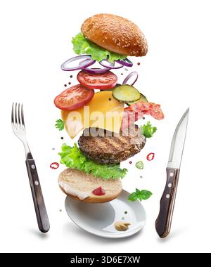 Cheeseburger ingredients with beef patty, vegetables and cheese floating in the air above a plate and cutlery next to it on a white background. File c Stock Photo