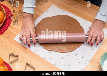 Making dough for Christmas cookies - gingerbread men, woman hands rolling out the dough with a hand rolling pin. Stock Photo