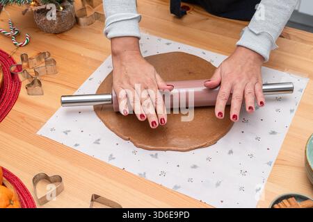 Making dough for Christmas cookies - gingerbread men, woman hands rolling out the dough with a hand rolling pin. Stock Photo